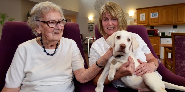 Resident June Lambley (left) with Home Manager Denise Morris and Charlie the puppy who is helping residents become more active copy