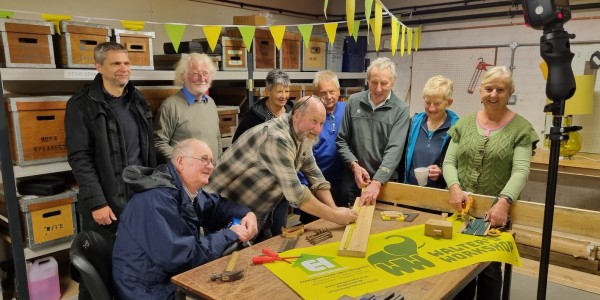 Caption: Chairman Alan Cheeseman measures some wood at Walter's Workshop during the official opening, surrounded by volunteers and Enterprise South West Manager Rob McKay, far left.