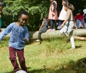 Children play football in an open wooded area.
