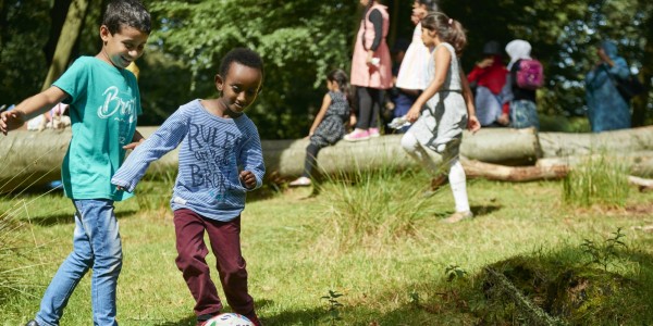 Children play football in an open wooded area.