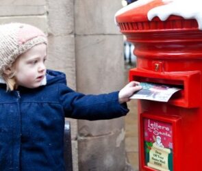 A young girl posts her letter to Santa in the special postbox.